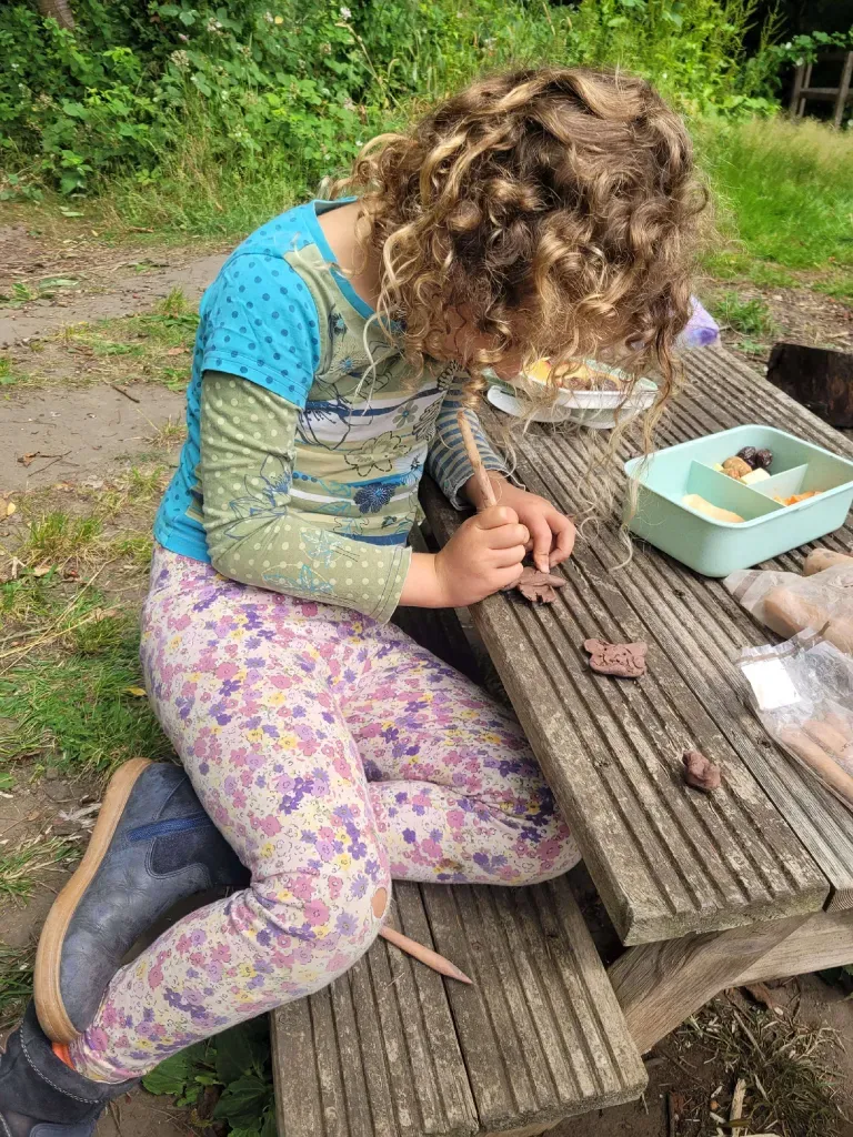 A child shaping small clay figures on a woodland workbench