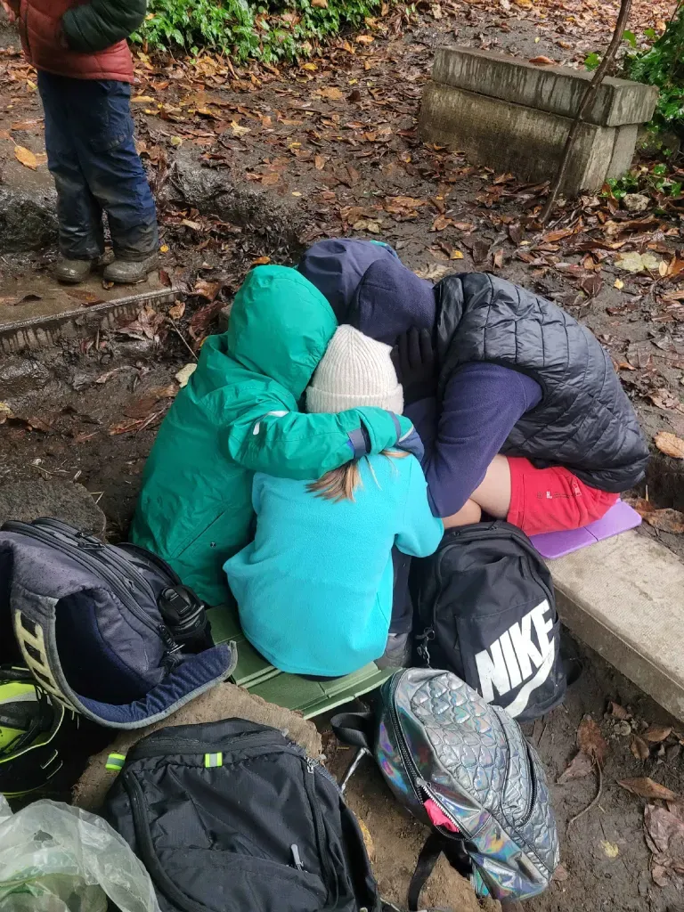 A close huddle of children in raincoats, heads together, sheltering and laughing on a wet day