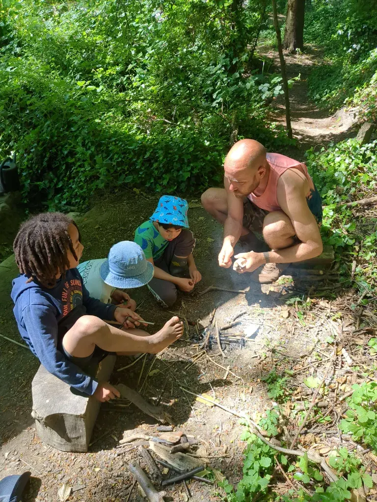 Close view of hands and boots around a small fire pit, mid-lesson