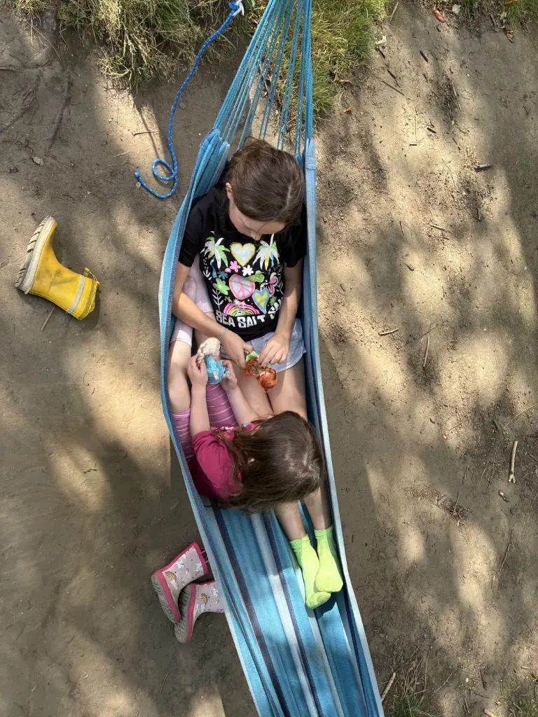 Two children sharing a hammock, looking down at something held between them