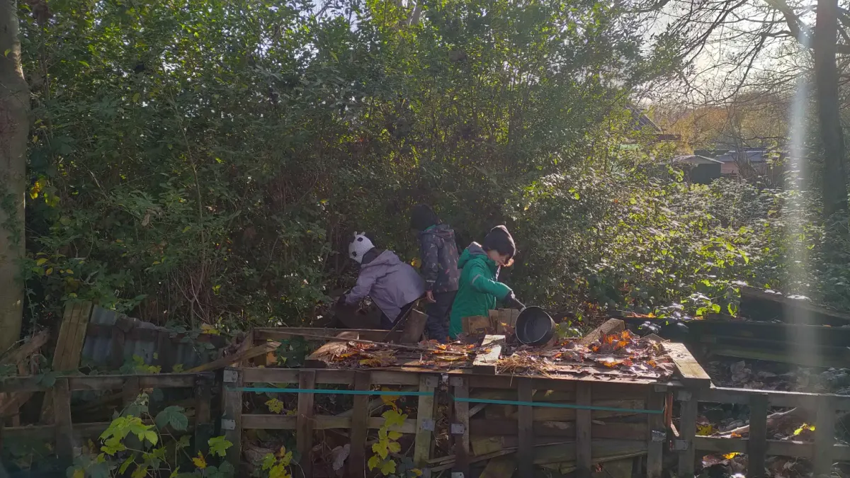 Children stirring leaves and mud in pots at an outdoor mud kitchen among the trees
