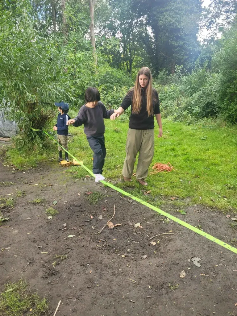 A child carefully balancing along a rope strung between trees, supported by an adult